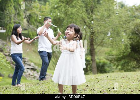 Eltern und Kinder blasen Seifenblasen im Park. Asiatische Familienaktivitäten im Freien Stockfoto