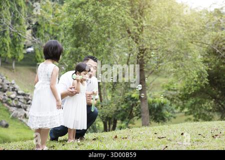 Eltern und Kinder blasen Seifenblasen im Gartenpark. Asiatische Familienaktivitäten im Freien Stockfoto