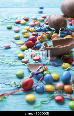 Foto von bunten Süßigkeiten, Schokoladeneiern auf blauem Holztisch Stockfoto