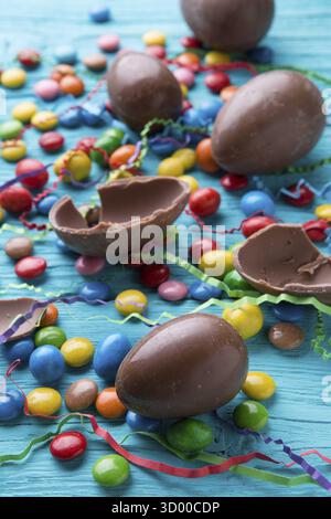 Fotohälften Schokoladeneier, bunte Süßigkeiten auf blauem Holztisch Stockfoto