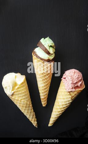 Eiscreme in Waffelform mit verschiedenen Geschmacksrichtungen auf einem schwarzen Brett. Vertikales Foto Stockfoto
