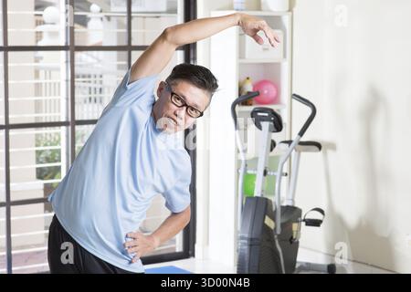 Porträt eines aktiven reiferen asiatischen Mannes aus den 50er Jahren in Sportbekleidung, der Arme dehnt und im Fitnessraum trainieren kann Stockfoto