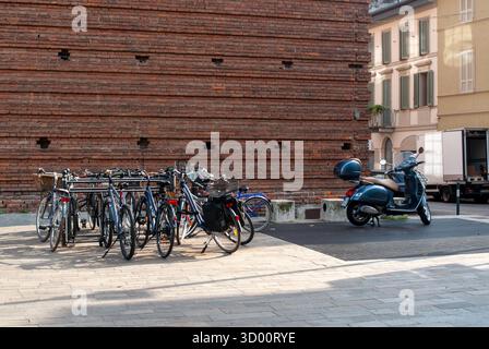 Cremona, Italien – 2. Oktober 2025 urbane Straßenszene mit mehreren Fahrrädern, die in einem Regal neben einem klassischen blauen Vespa-Roller geparkt sind Stockfoto