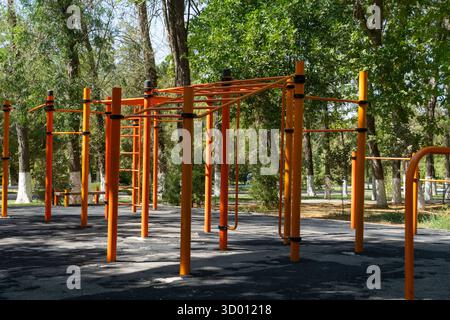 Outdoor-Fitnesspark mit orangefarbenen Metallbars, Pull-up-Stationen und von Bäumen umgebenen Affenbars, die einen gesunden Lebensstil und ein öffentliches Fitness fördern Stockfoto