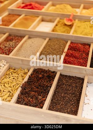 Bunte Gewürze sind in Holztabletts an einem Marktstand ordentlich angeordnet. Die lebhafte Auswahl umfasst eine Vielzahl von Texturen und Aromen, Attrac Stockfoto