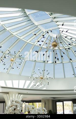 Ein geräumiger Raum verfügt über eine wunderschöne Glasdecke, in der natürliches Licht einströmen kann. Moderne Leuchten verleihen der Atmosphäre einen Hauch von Eleganz Stockfoto
