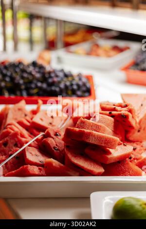 Ein lebhaftes Sortiment an frisch geschnittenen Wassermelonenscheiben wird am Sommerbuffet serviert, zusammen mit Blaubeeren und anderen Früchten, die ein Colorfu bilden Stockfoto