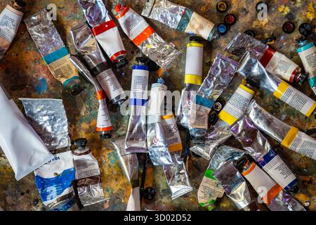 Nahaufnahme von oben auf zahlreiche farbenfrohe Farbröhren, die in einem Künstlerstudio auf einer unordentlichen Arbeitsfläche verstreut sind. Stellt den kreativen Prozess dar Stockfoto