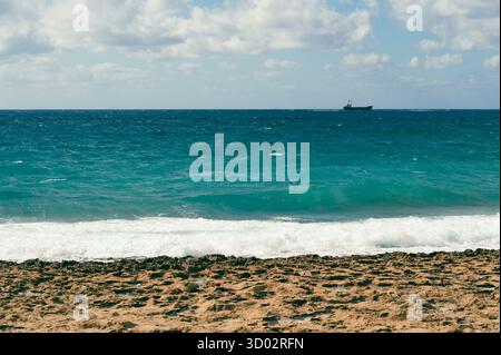 Eine atemberaubende Aussicht auf einen ruhigen Strand mit sanften Wellen und einem entfernten Boot unter einem teilweise bewölkten Himmel Stockfoto