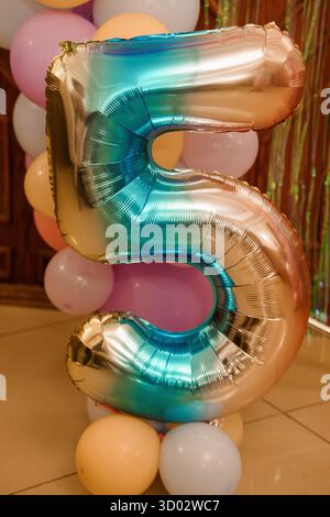 Ein großer, silberfarbener Folienballon mit der Zahl 5 mit Farbverlauf steht prominent zwischen einer Gruppe pastellfarbener Ballons, perfekt für Geburtstagsfeiern und fe Stockfoto