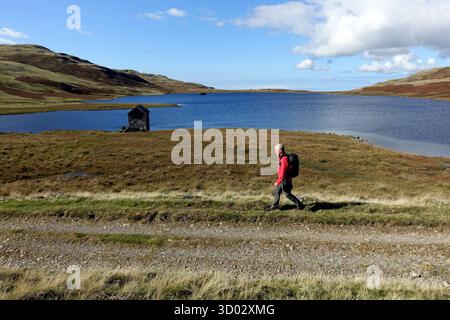 Single man (Wanderer) Walking on Track by the Boathouse on Devoke Water im Lake District National Park, Cumbria, England, Großbritannien. Stockfoto