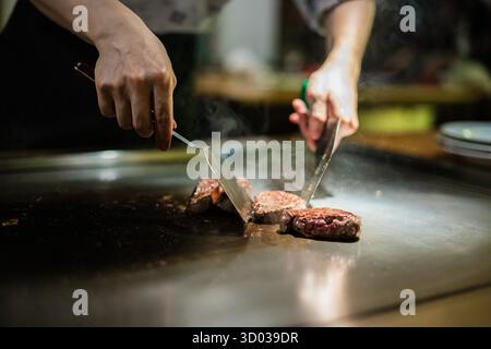 Teppanyaki, japanische Teppanshow in traditionellem Restaurant. Hände des Kochs. Der Koch bereitet Fleisch, Fisch, Reis und Gemüse auf einem heißen Tisch vor den Gästen zu. Küche Völker der Welt Konzept Stockfoto