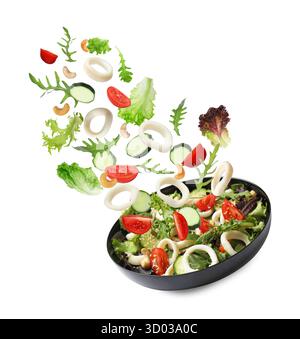 Tintenfischringe und andere Zutaten, die in eine Schüssel mit Salat vor weißem Hintergrund fallen Stockfoto
