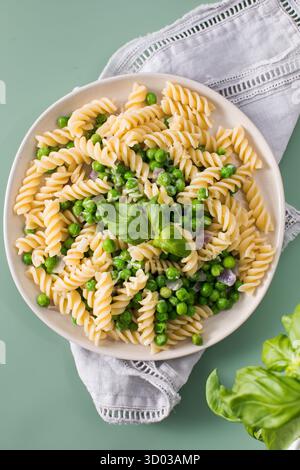 Fusilli-Pasta mit gedämpften Erbsen und Basilikum, serviert auf Tellern. Köstliches gesundes veganes Gericht mit Naturprodukten auf grünem Tisch. Gourmet-Abendessen Stockfoto