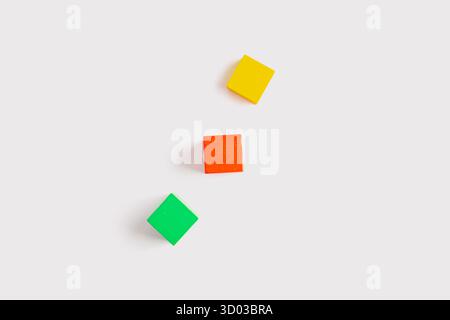 Drei bunte Holzwürfel, gelb, rot und grün, diagonal auf einem sauberen weißen Hintergrund in einer minimalen und geometrischen flachen Lage angeordnet. Stockfoto