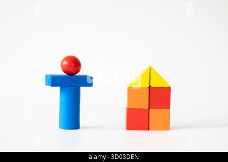 Kreative Komposition aus bunten Holzblöcken, die neben einer Hausform auf weißem Hintergrund eine menschliche Figur bilden und die Familie, das Haus oder die frühe E symbolisieren Stockfoto