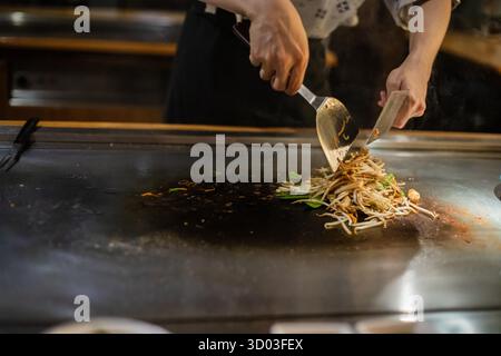 Teppanyaki, japanische Teppanshow in traditionellem Restaurant. Hände des Kochs. Der Koch bereitet Fleisch, Fisch, Reis und Gemüse auf einem heißen Tisch vor den Gästen zu. Küche Völker der Welt Konzept Stockfoto