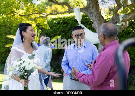Braut mit Blumenstrauß lächelt und plaudert mit Gästen bei einer Hochzeit im Freien. Feier, Blumen, draußen, Glück, Unterhaltung || Model veröffentlicht Stockfoto