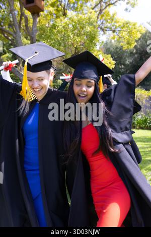 Absolventen in Mützen und Kleidern, die gemeinsam im Freien fröhlich feiern. Abschluss, Feier, Erfolg, Universität, College, Happiness || Model veröffentlicht Stockfoto