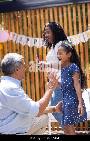 Großvater spielt mit Enkelin, Mutter lächelt auf einer Geburtstagsparty im Freien. Familie, Feier, Glück, draußen, Picknick, Multigenerational || Modell veröffentlicht Stockfoto