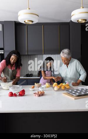 Drei Generationen backen gemeinsam Cupcakes in moderner Küche und genießen die Familienzeit. Bonding, Inland, Kulinarik, Lifestyle, Teamwork || Model veröffentlicht Stockfoto