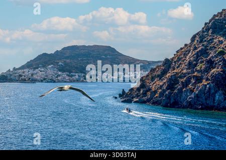 Seagull fliegen über den Eingang zum Skala Port in Patmos, mit dem Weißen Dorf und den Rocky Hills, Griechenland Stockfoto