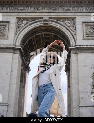 Fröhliche Frau in lässigem Outfit in der Nähe des Arc de Triomphe in Paris, Frankreich, mit erhobenen Händen an einem Sommertag || Model veröffentlicht Stockfoto