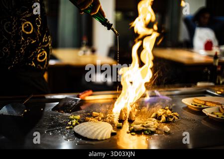 Teppanyaki, japanische Teppanshow in traditionellem Restaurant. Hände des Kochs. Der Koch bereitet Fleisch, Fisch, Reis und Gemüse auf einem heißen Tisch vor den Gästen zu. Küche Völker der Welt Konzept Stockfoto