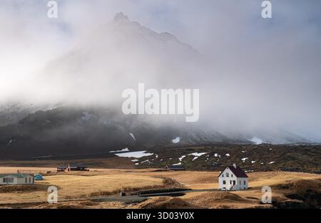 Einsames schönes Haus im kleinen Fischerdorf Arnarstapi und schneebedeckte Bergklippe auf der Snaefellsness-Halbinsel in Island Stockfoto