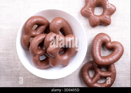 In Schokolade getauchter Lebkuchen, in einer weißen Schüssel, auf Leinen. Herz- und sternförmige traditionelle deutsche Lebkuchen, komplett mit Milchschokolade überzogen. Stockfoto
