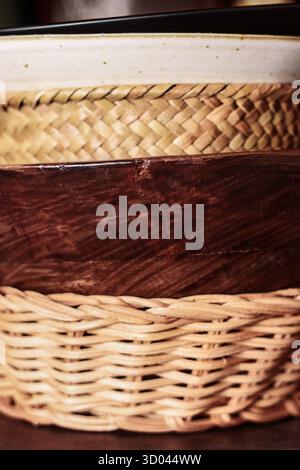 Stapel rustikaler Keramik- und Holzgeschirr auf Küchenregal. Teller, Korbschalen mit natürlichen Texturen. Handgefertigtes Detail-Konzept Stockfoto