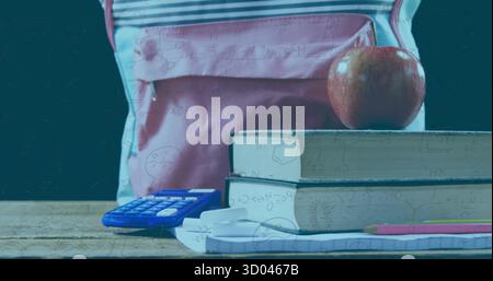 Auf dem Schreibtisch mit rotem Apfel und Ohrhörern befindet sich ein hellrosafarbener Rucksack, der sich hinter Schulutensilien versteckt Stockfoto