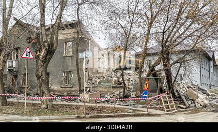 Verlassenes Gebäude mit erheblichen strukturellen Schäden, Trümmern und Baumaschinen in der Nähe, die eine Szene von bilden Stockfoto