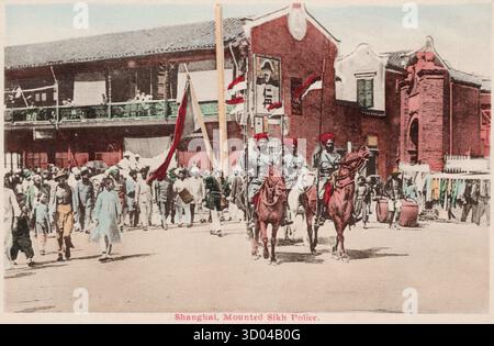 Ansichtskarte aus dem frühen 20. Jahrhundert von der berittenen Sikh-Polizei zu Pferd, die während der Konzessionszeit in China eine überfüllte Straße in Shanghai patrouillierte. Nicht identifizierter Fotograf Stockfoto