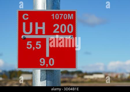Nahaufnahme eines roten reflektierenden Hinweistafels zur Lage des Hydranten, das auf einem galvanisierten Metallmast vor einem hellblauen Hintergrund des Himmels montiert ist Stockfoto