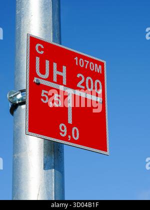 Nahaufnahme eines roten Positionsschilds für Hydranten mit reflektierenden Markierungen, die an einem Metallbeleuchtungsposten gegen einen klaren blauen Himmel für den Notfall angebracht sind Stockfoto