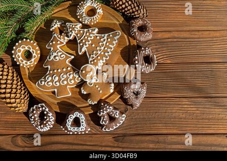 Festliche Lebkuchenkekse auf Holztisch. Dekorierte Lebkuchenkekse und Schokoladengerichte auf einer Holzplatte mit Tannenzapfen und Stockfoto