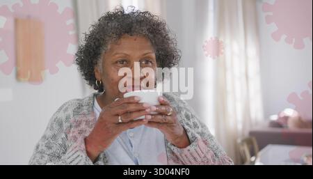 Eine ältere Frau mit blauer Bluse und Strickjacke am Esstisch, mit Keramikbecher Stockfoto