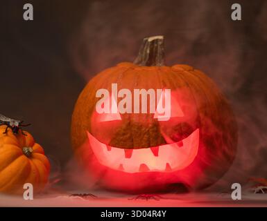 Gruseliger Halloween Kürbis mit leuchtenden roten Augen und Rauch auf schwarzem Hintergrund Stockfoto