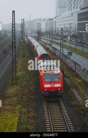 Ein roter DB-Zug fährt an einem nebeligen Wintertag auf Gleisen in einem städtischen Gebiet Stockfoto