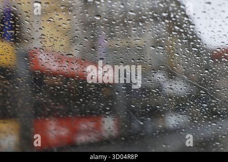 Regentropfen auf Glas mit verschwommenen Gebäuden und roten Autos im Hintergrund der Stadt Stockfoto