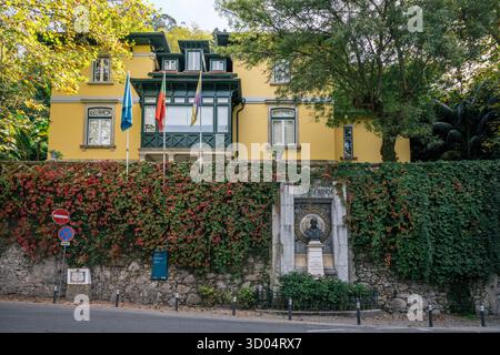 Gelbes historisches Gebäude mit grünen Details und einem Steindenkmal, das am 16. Oktober in Sintra, Lissabon, Portugal, vor einer mit Efeu bedeckten Mauer steht. Stockfoto