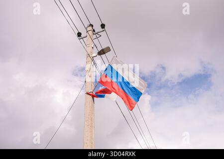 Russland, Sankt Petersburg, 23.08.2025 zwei Fahnen mit roten, blauen und weißen Streifen, die von einem elektrischen Pol mit Stromleitungen und einer Straßenlampe aga winken Stockfoto