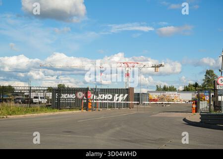 Russland, Sankt Petersburg, Baustelleneingang 23.08.2025 mit einem großen Kran, der über die Barriere hinausragt, und einem klaren blauen Himmel. Industrielle Entwicklung Stockfoto