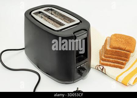 Schwarzer elektrischer Toaster mit braunen Brotscheiben auf Küchentuch, Konzept des Frühstücks und Hausmannskost Stockfoto