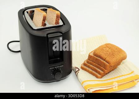 Schwarzer elektrischer Toaster mit braunen Brotscheiben auf Küchentuch, Konzept des Frühstücks und Hausmannskost Stockfoto
