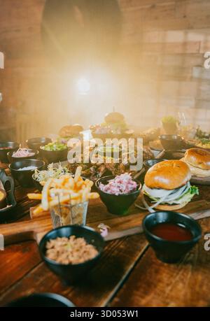 Ein Tisch voller Speisen, einschließlich einer Vielzahl von Sandwiches, Pommes und anderen Beilagen. Die Szene ist einladend und appetitlich Stockfoto