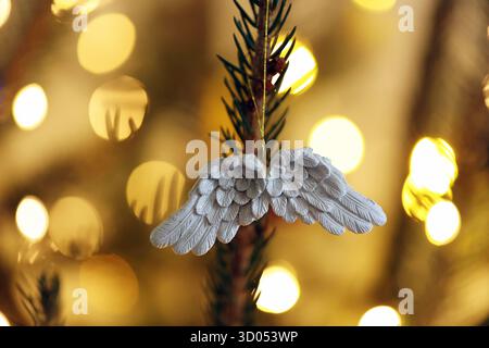 Nahaufnahme eines weißen Engelsflügels, der an einem Weihnachtsbaum hängt, mit warmen Bokeh-Lichtern im Hintergrund Stockfoto