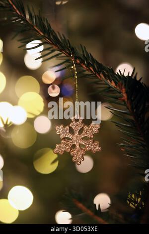 Glitzernde Schneeflocken-Ornamente hängen an einem Weihnachtsbaum mit hellen, warmen Bokeh-Lichtern im Hintergrund Stockfoto