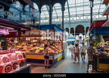 Menschen gehen an einer farbenfrohen Auslage eines frischen Obststands auf dem lebhaften Atarazanas-Lebensmittelmarkt in Málaga, Spanien, vorbei. Stockfoto